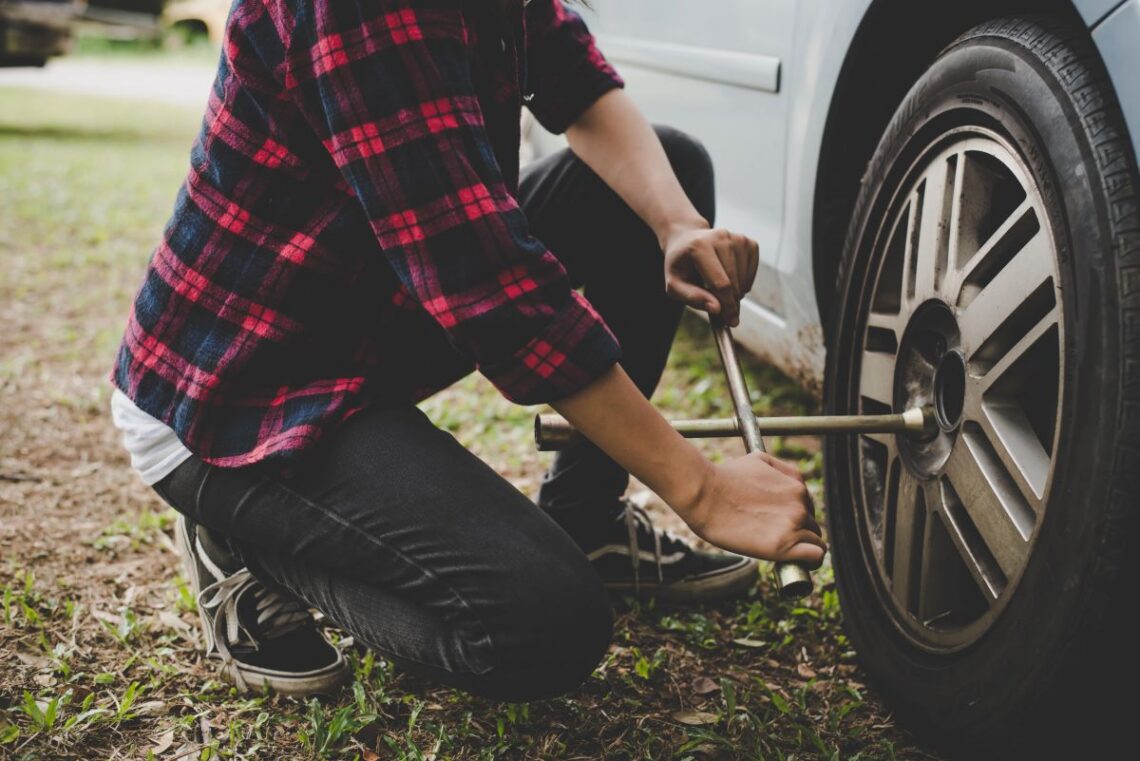 Person in red and black plaid changing a car tire