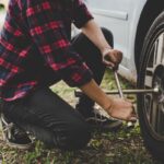 Person in red and black plaid changing a car tire