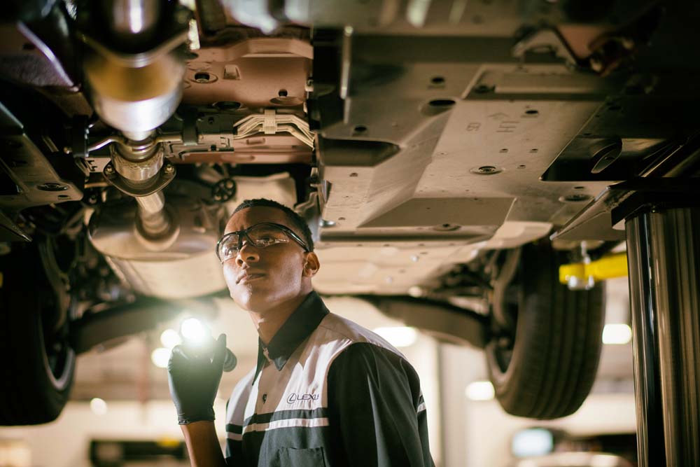 Lexus technician inspecting hybrid battery under car